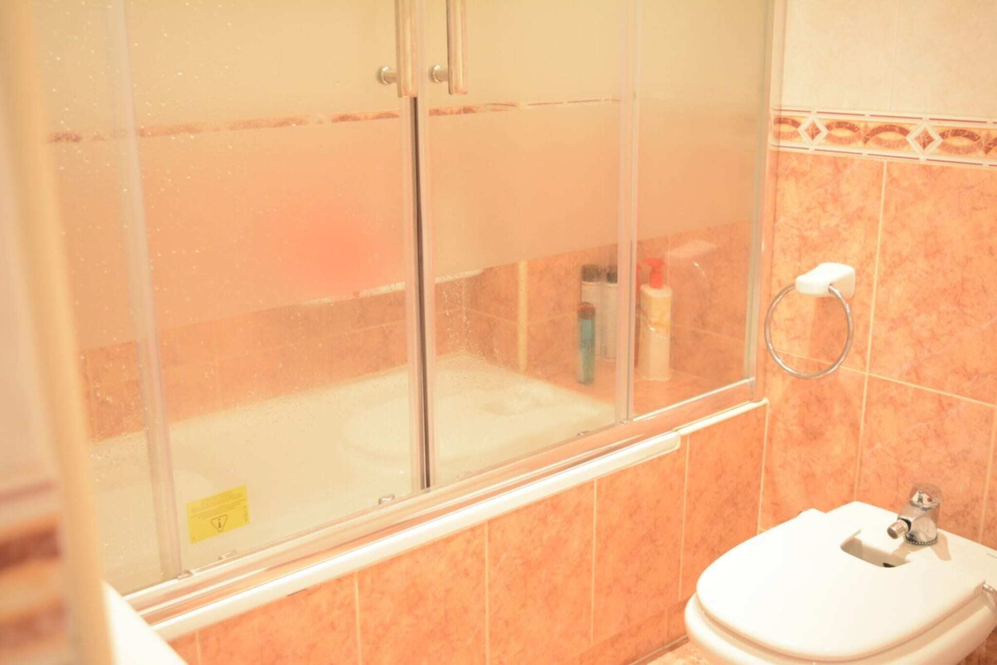A bathroom with a glass shower enclosure, a toilet, and a sink.