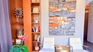 Un área de recepción moderna con una pared de piedra, dos sillas blancas, una mesa redonda y una planta en maceta.