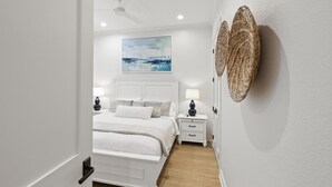 Un dormitorio con cama, mesitas de noche, ventilador de techo, un cuadro y decoración mural tejida.