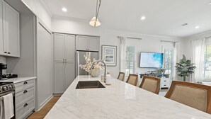 Una cocina moderna con una isla de mármol, armarios blancos y un comedor con sillas.