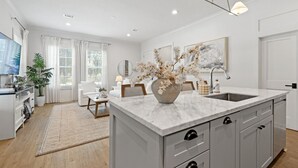 Una cocina moderna con una isla de mármol, un área de comedor con un sofá blanco y un amplio ventanal con cortinas.