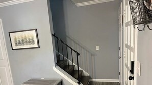 A staircase with a black railing, a small table with a wire shelf, and a framed picture on the wall. - On Island | Pool | Tennis | Pet Friendly | Parking (Hilton Head Island)