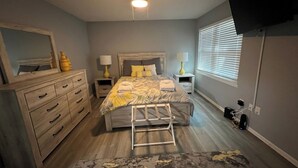 A bedroom with a bed, nightstands, a dresser, a ceiling fan, a window with blinds, and a television mounted on the wall. - On Island | Pool | Tennis | Pet Friendly | Parking (Hilton Head Island)