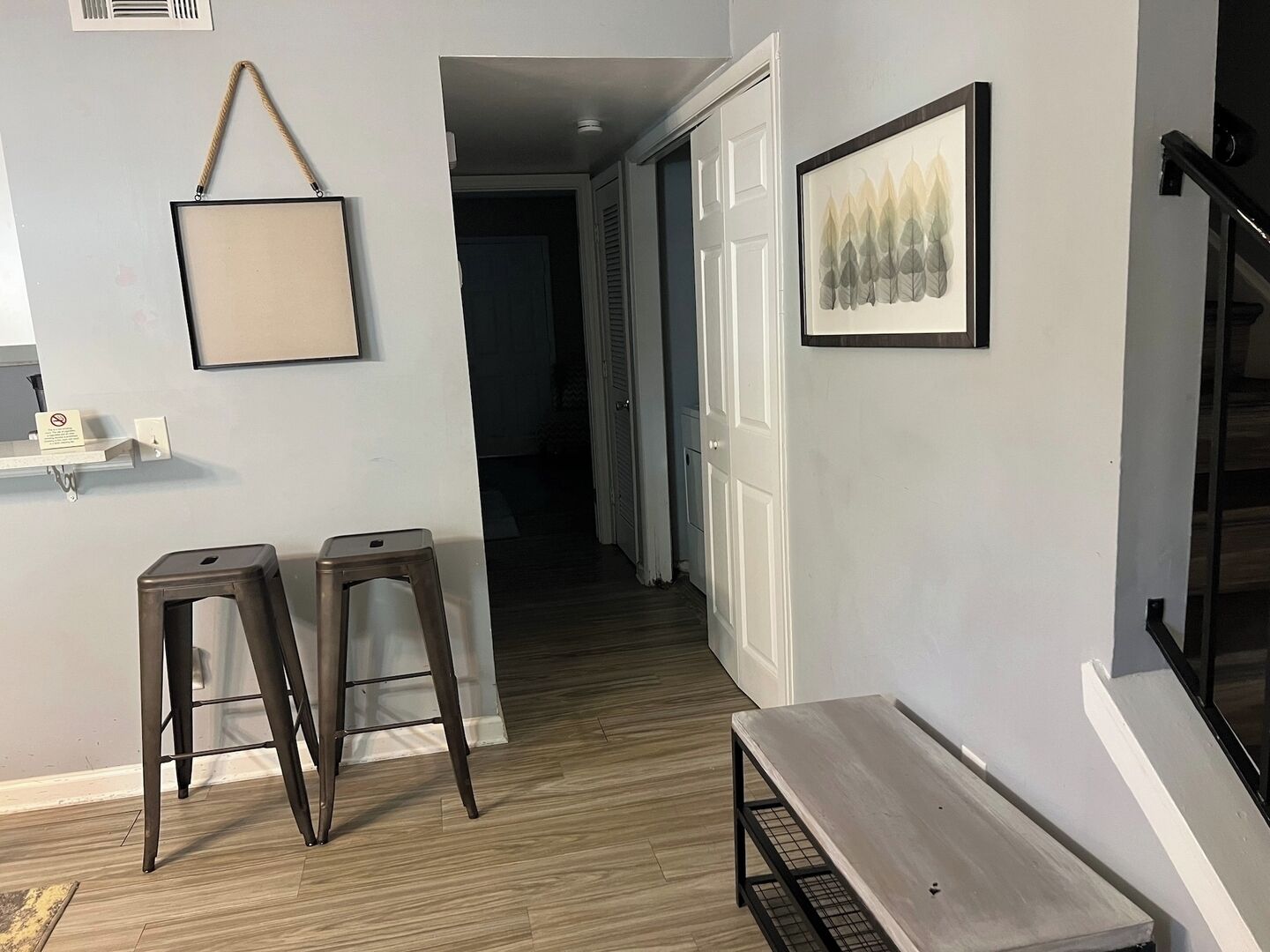 A hallway with a bench, two stools, a framed picture, and a door leading to another room.