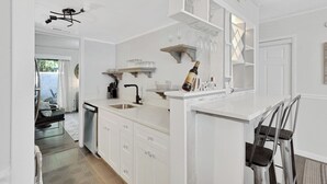 Una cocina moderna con armarios blancos, pileta integrada y una barra con vasos y botellas.