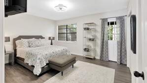 Un dormitorio con cama, mesita de noche, lámpara, ventana con persianas y puerta con cortinas.