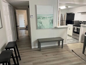 Uma cozinha moderna com eletrodomésticos de aço inoxidável, sala de jantar com bancos e corredor que dá para outro quarto.
