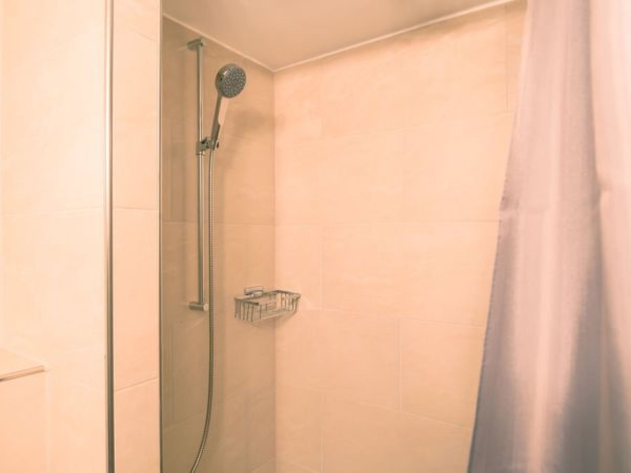 A shower with a handheld showerhead and a wall-mounted faucet, a glass shower enclosure, and a shower caddy.