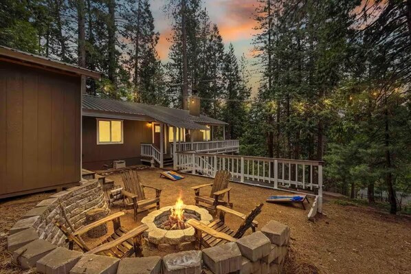 Una cabaña con terraza, un hoyo para la fogata y vistas al bosque.