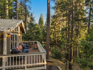 Una cabaña con terraza, mobiliario exterior y un bosque de fondo.