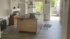 Une cuisine moderne avec des meubles en bois, un îlot central, des ustensiles de cuisine suspendus et une vue sur l’extérieur.