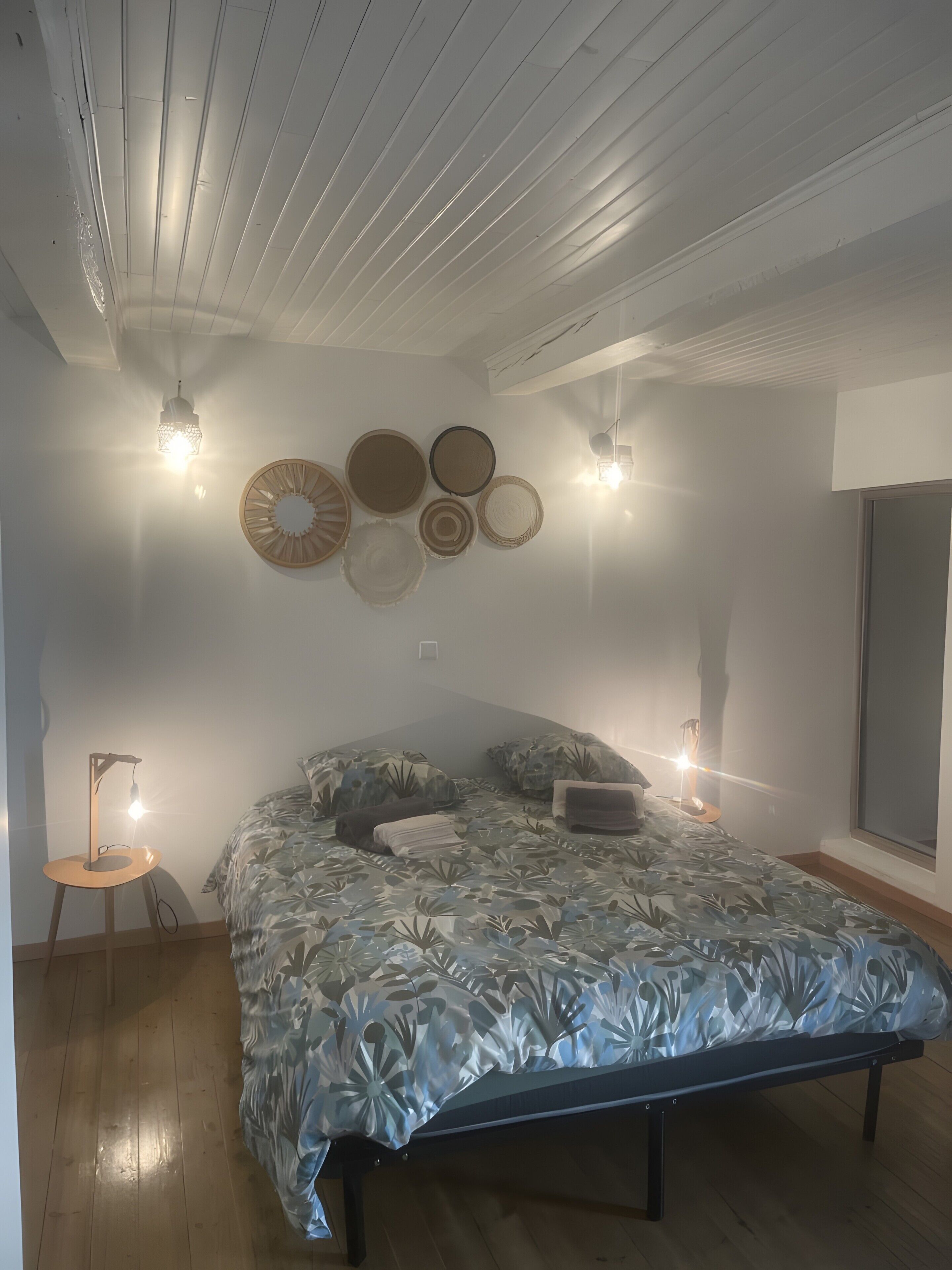 Un dormitorio con cama, luces fijadas a la pared y un ventanal grande.