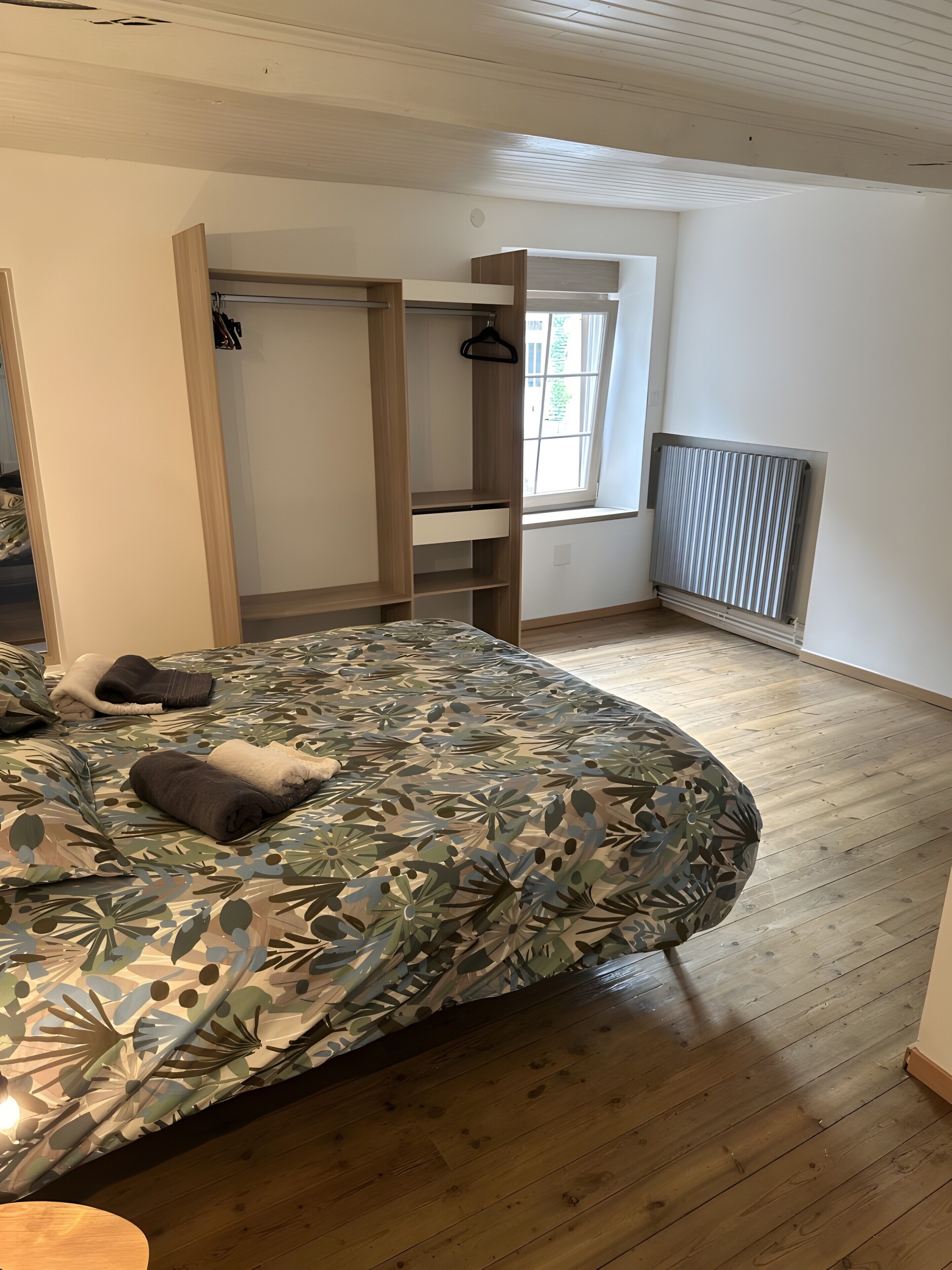 A bedroom with a bed, a wardrobe, a radiator, and a window.