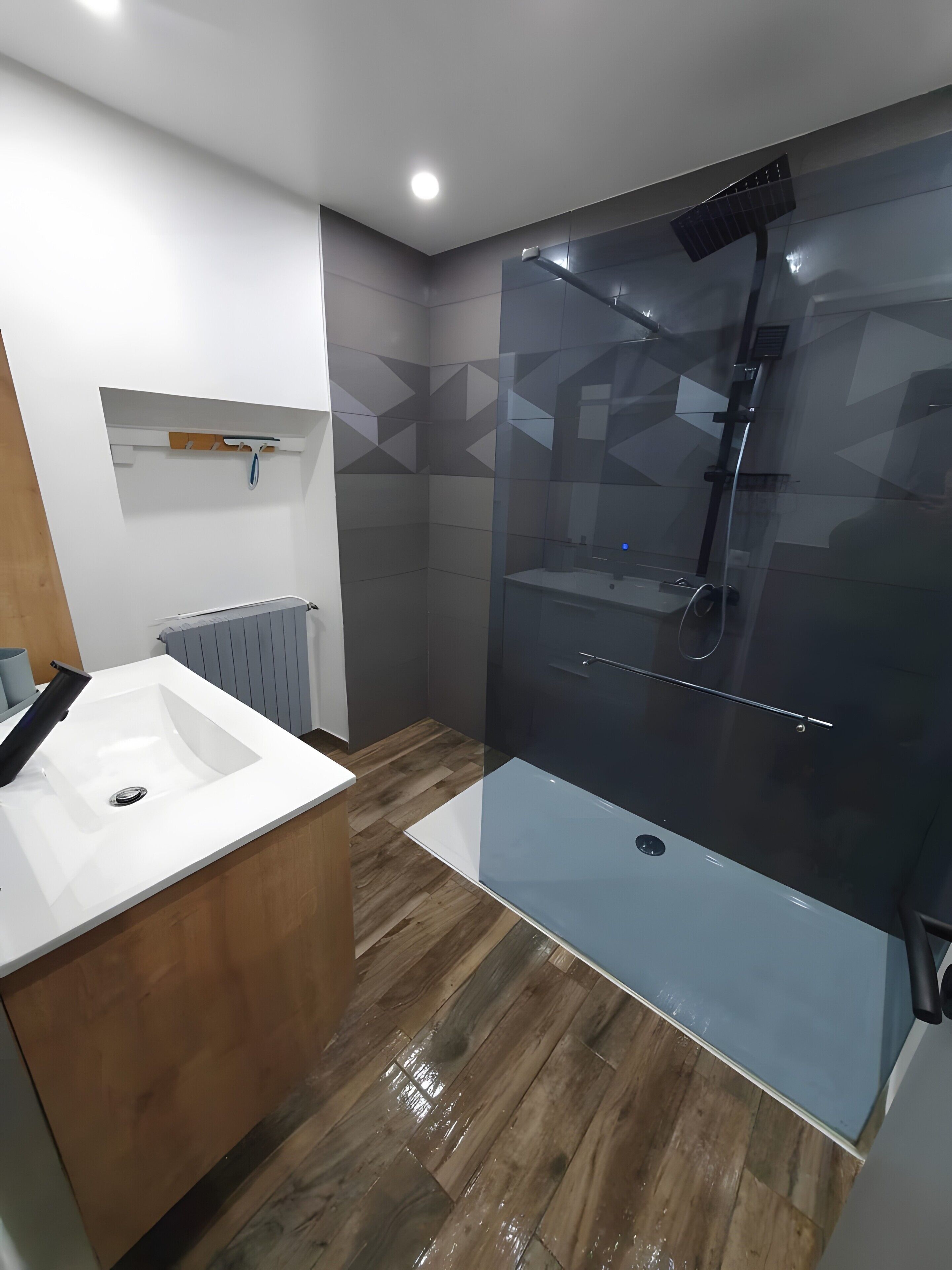 A modern bathroom with a glass-enclosed shower, a white sink, and a wooden vanity.