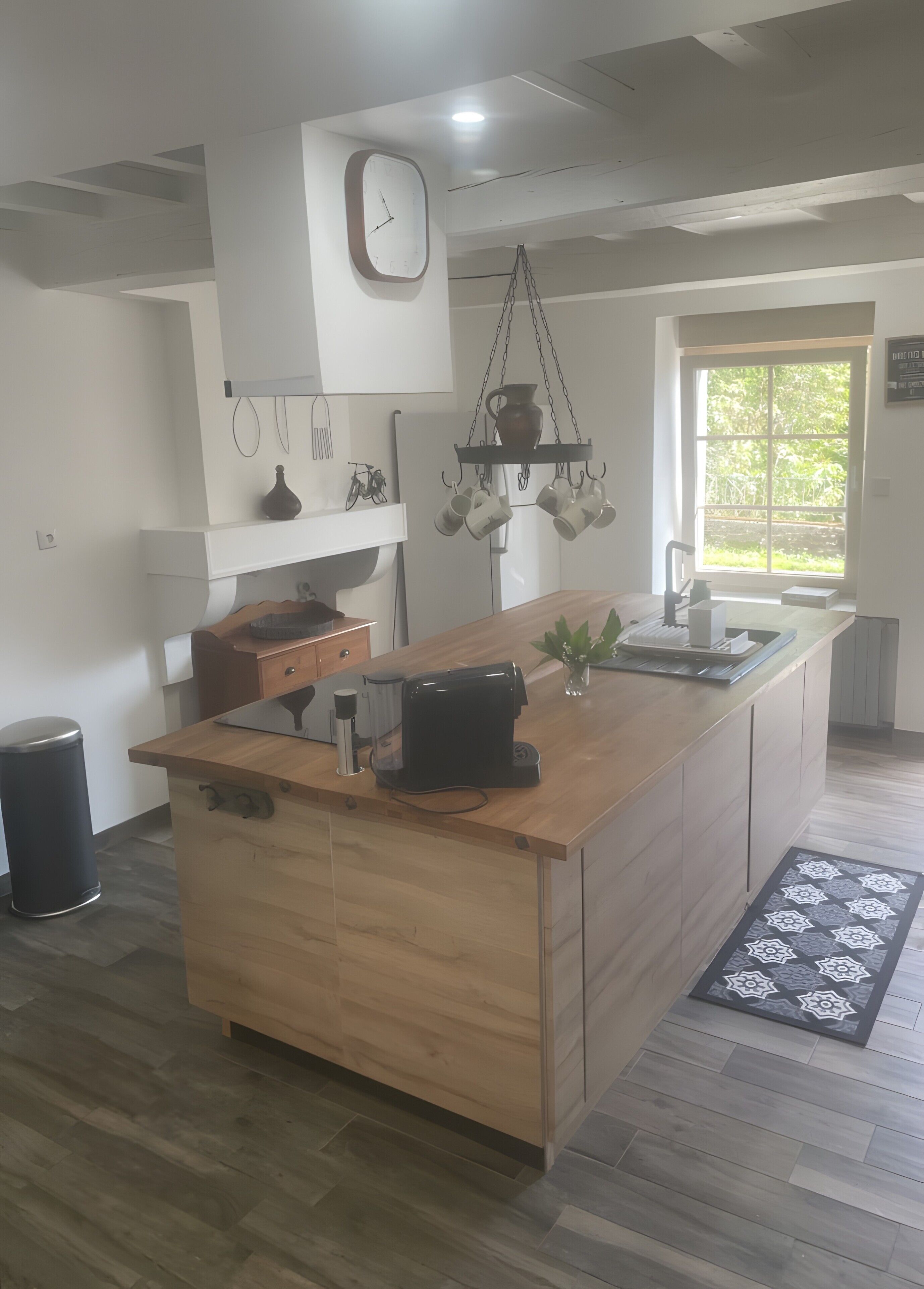 Een moderne keuken met een houten kookeiland, een hangende rek voor pannen en een groot raam.