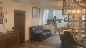 Un salon doté d’un parquet, d’un canapé en cuir noir, d’un meuble en bois et d’un coin repas avec une table et des chaises.