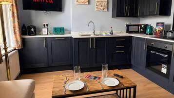 A modern kitchen with dark cabinets, a flat-screen TV displaying 'NETFLIX,' a coffee maker, a kettle, and a microwave.