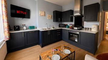 A compact kitchen with a built-in oven, microwave, and coffee maker. A dining table with cutlery is set in the center.