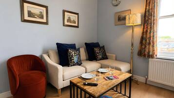 Ein Wohnzimmer mit Sofa, Sessel, Couchtisch, gerahmten Bildern und einer Lampe.