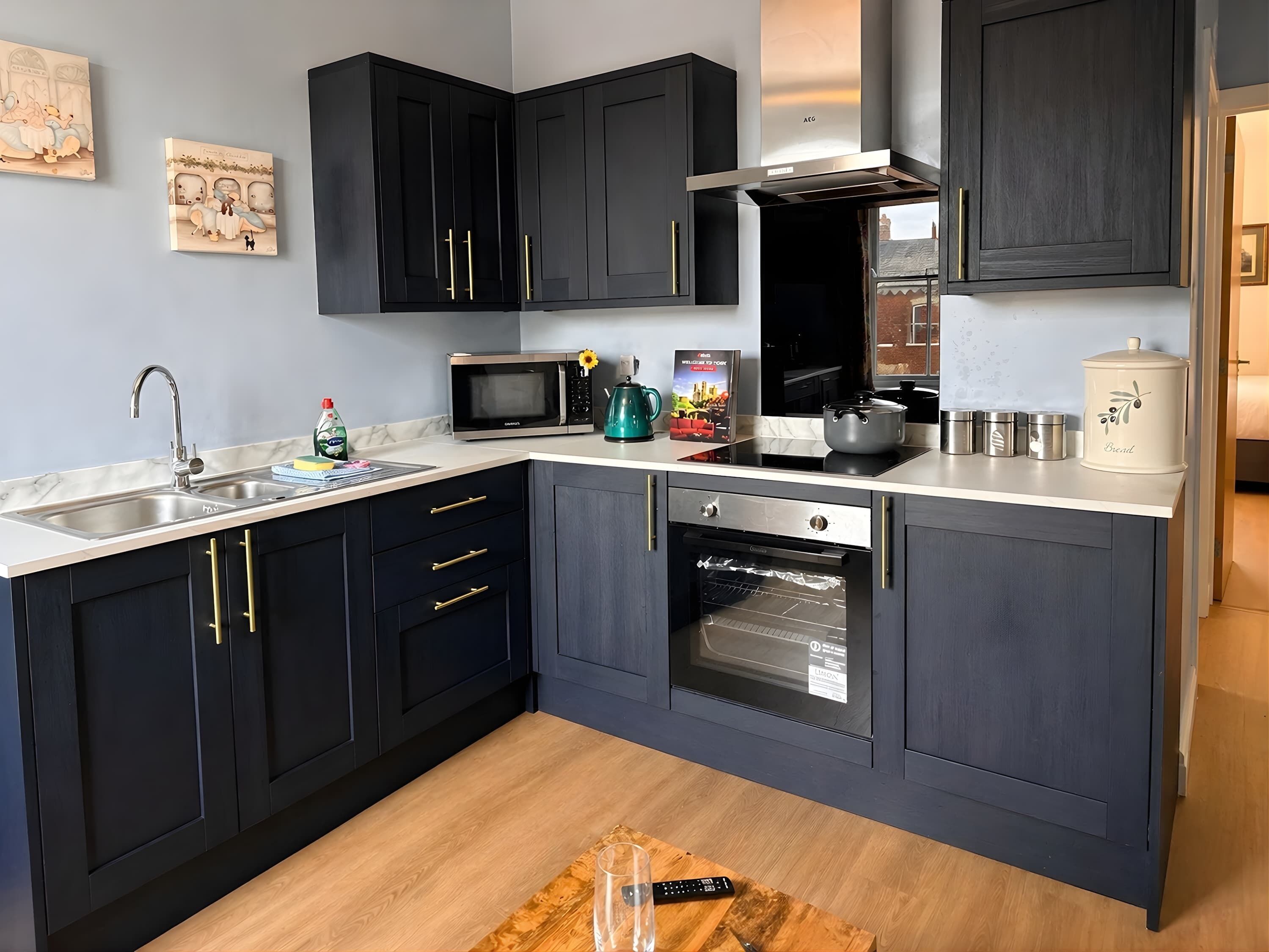 A modern kitchen with dark cabinetry, a stainless steel sink, a microwave, an oven, and a coffee maker.