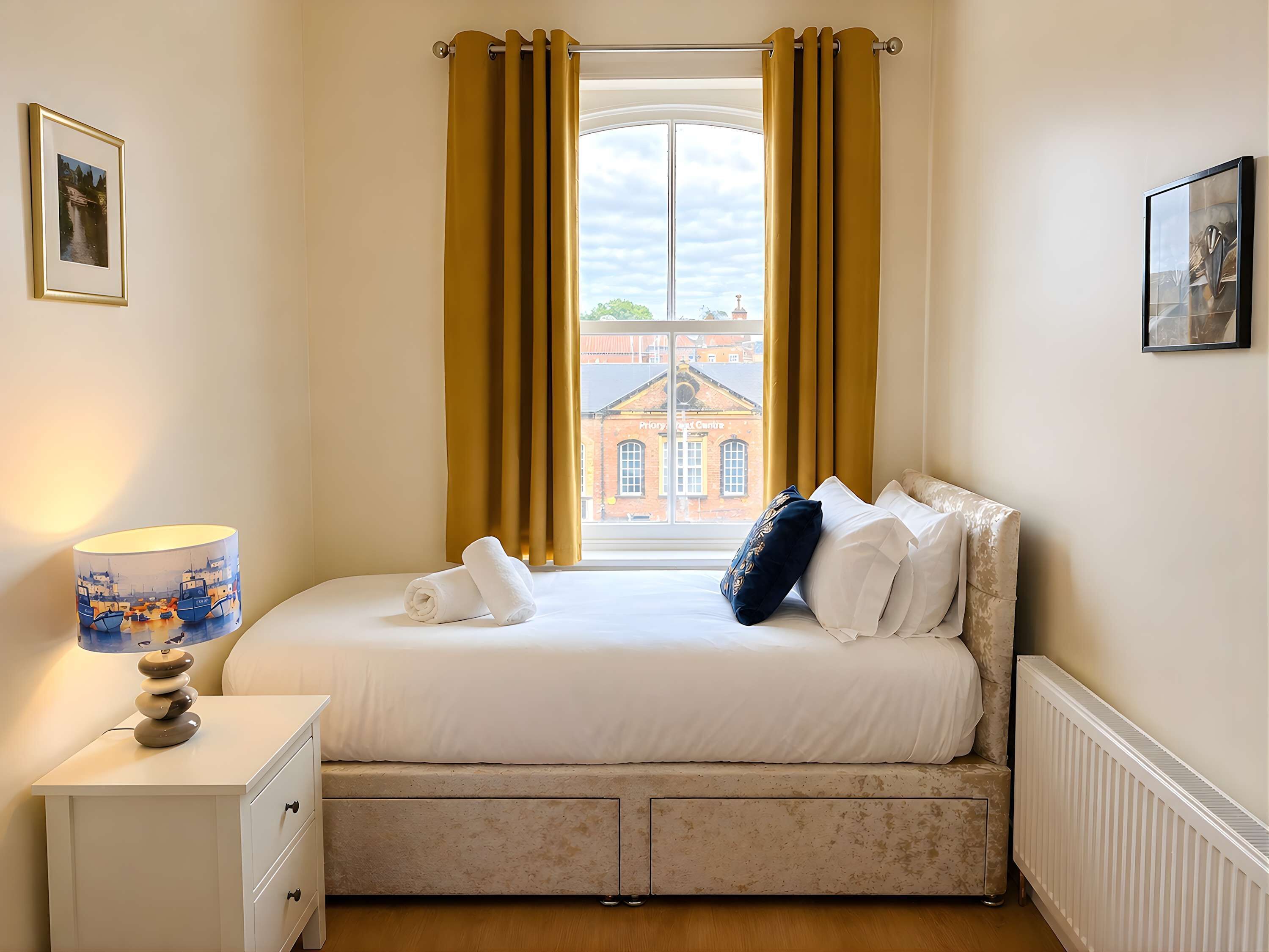 A bedroom with a bed, a nightstand, a lamp, and a window with curtains.