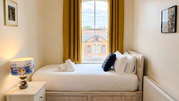 A bedroom with a bed, a nightstand, a lamp, and a window with curtains.
