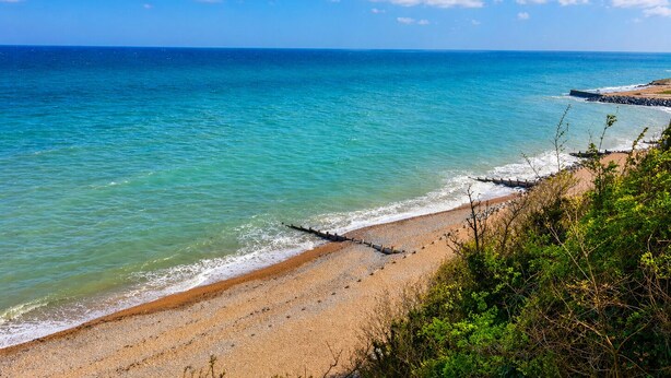 Een strand met helder turquoise water, een zandstrand en een rotsenrij.