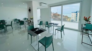 Un comedor moderno con mesas y sillas, un ventanal con vistas a la ciudad y un equipo de aire acondicionado instalado en la pared.
