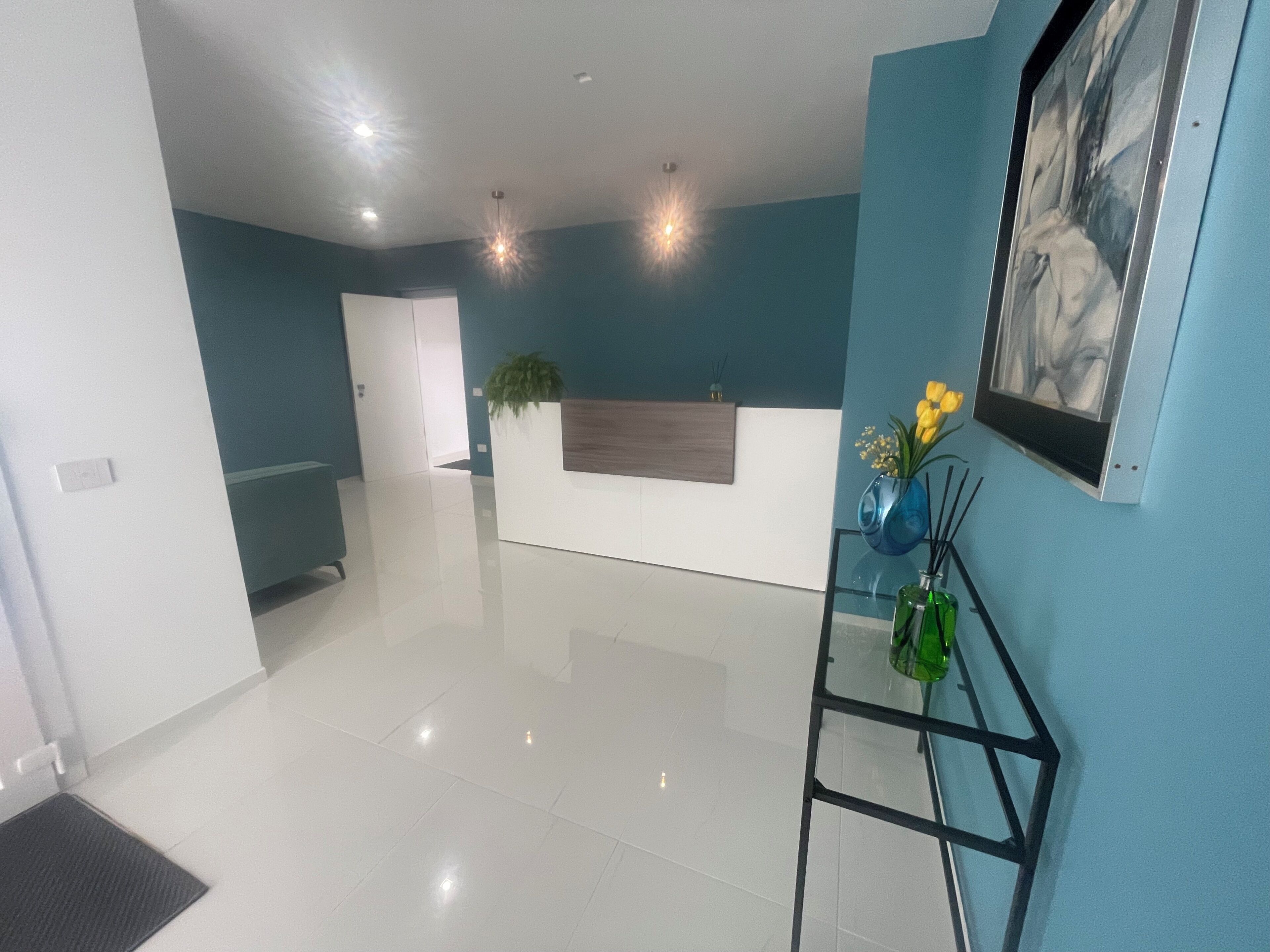 A modern reception area with a white reception desk, a blue wall, and a glass display cabinet with flowers.