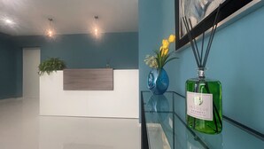 Una recepción con una planta, un florero con flores y una botella de perfume sobre una mesa de vidrio.