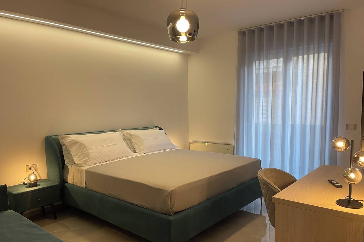A modern bedroom with a bed, bedside table, lamp, and a desk with a chair.