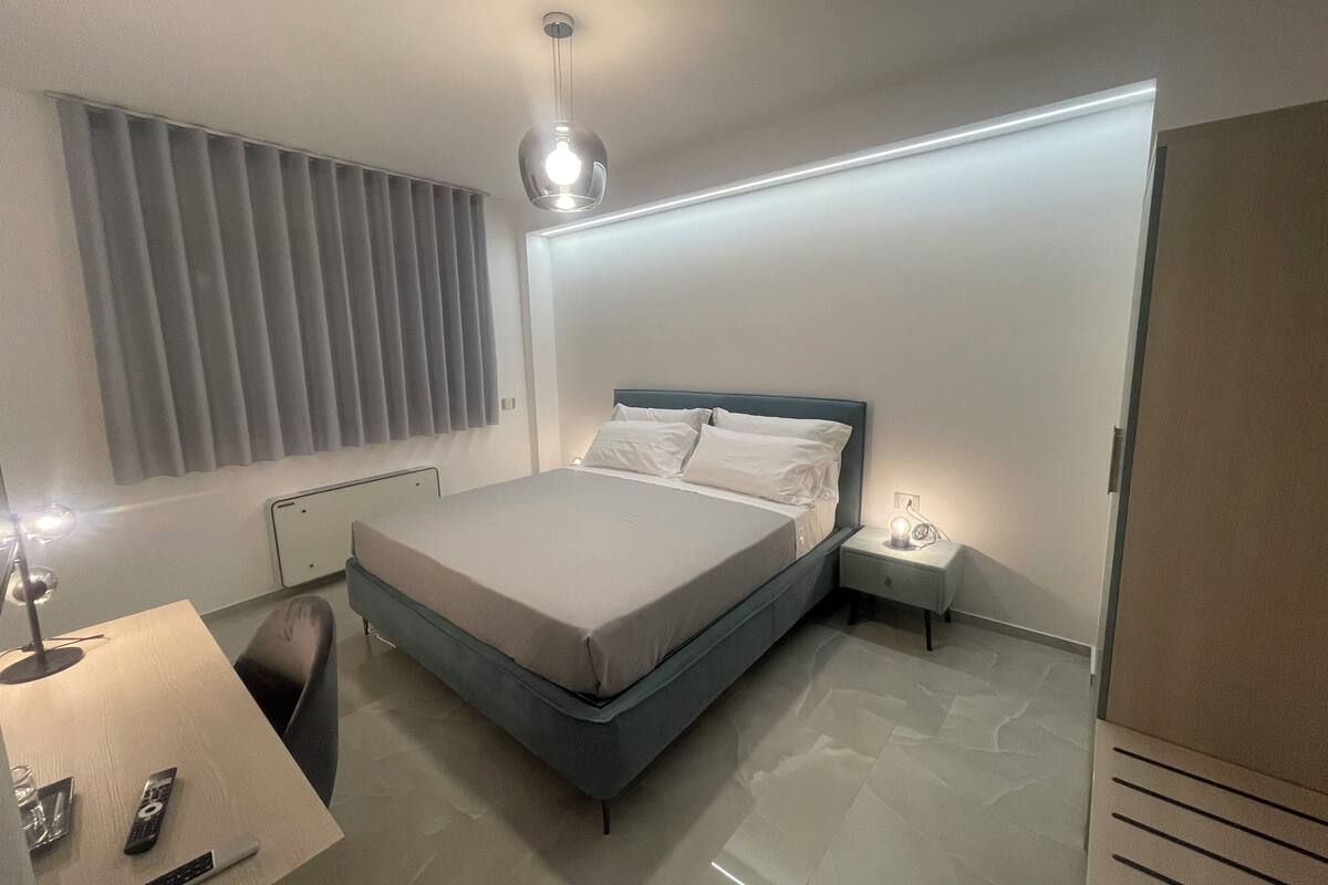 A modern bedroom with a bed, bedside table, lamp, and a desk with a chair.