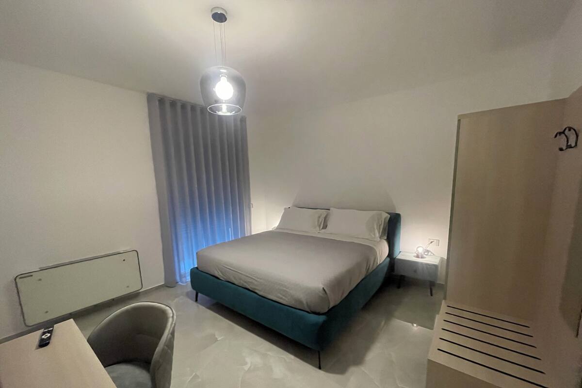 A modern bedroom with a bed, a chair, a desk, and a wardrobe.