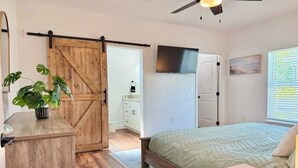 A bedroom with a bed, a wooden dresser, a sliding barn door, a ceiling fan, and a window with blinds. - Starfish - Tremendous 2-bedroom house with AC in Punta Gorda (Punta Gorda)