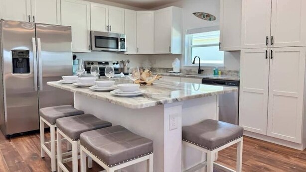 A kitchen with white cabinets, a stainless steel refrigerator, a microwave, a marble island with bar stools, and a sink. - Starfish - Tremendous 2-bedroom house with AC in Punta Gorda (Punta Gorda)