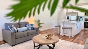 A modern living room with a grey sofa, a round wooden coffee table, and a kitchen area with white cabinets and a central island. - Starfish - Tremendous 2-bedroom house with AC in Punta Gorda (Punta Gorda)