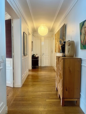 Ein Flur mit Holzboden, weißen Türen, einem Holzschrank und einer Pendelleuchte.