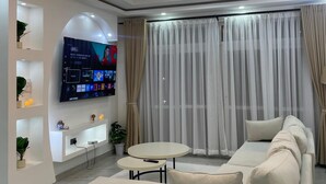 Un soggiorno moderno con una TV a schermo piatto, un lampadario, una ventola a soffitto e un divano.