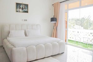 A bedroom with a large bed, a painting on the wall, a lamp, and a view of the outdoors. - Marvelous apartment with AC in peaceful Mombasa neighborhood (Mombasa)