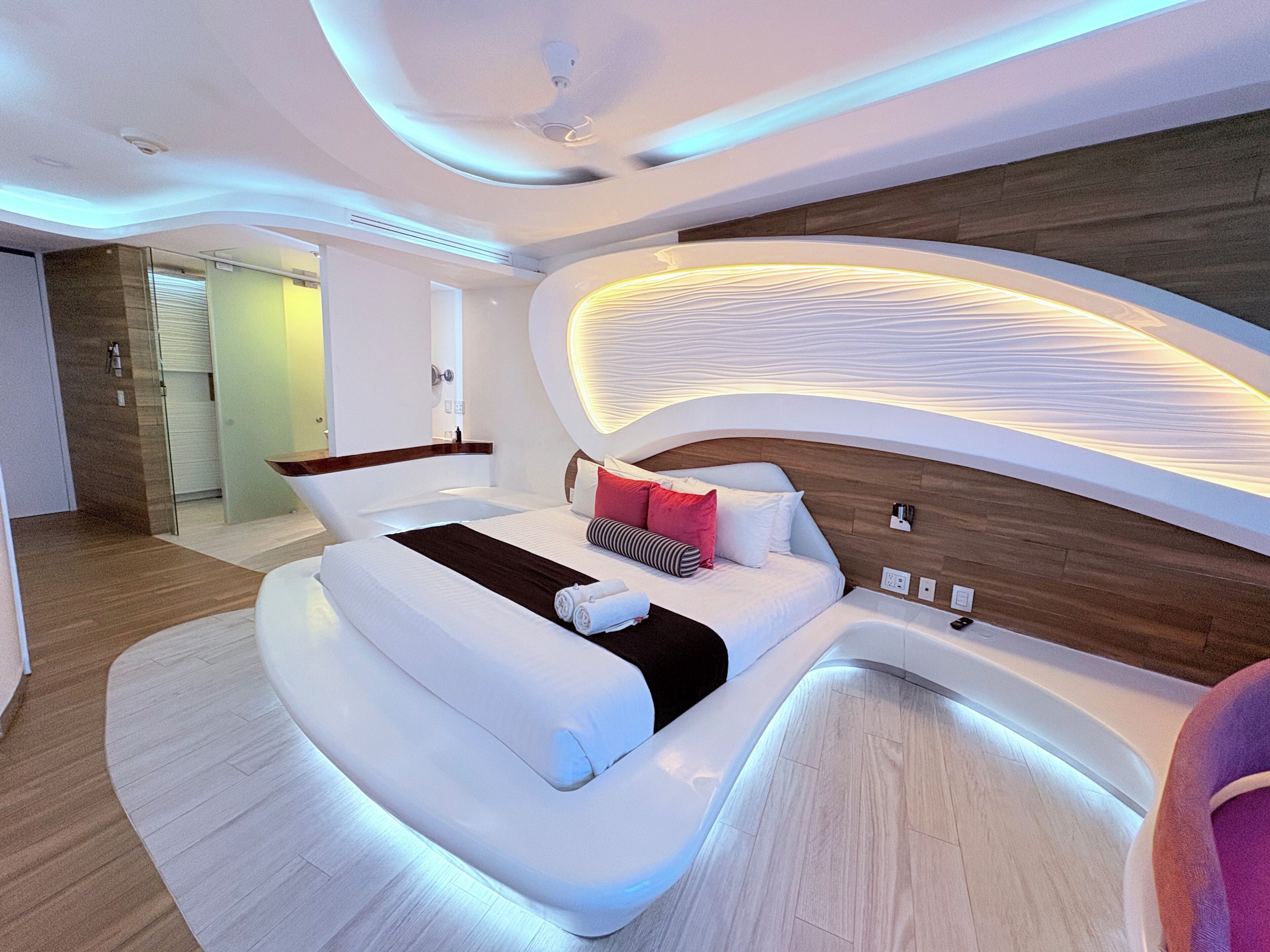 A modern bedroom with a curved bed, recessed lighting, and a wooden headboard.
