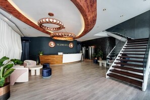 Eine moderne Hotellobby mit einer Rezeption, einer Treppe und einer großen Holzzieldecke.