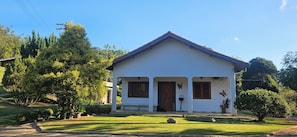 Una casa blanca de un solo piso con techo rojo, rodeada de follaje y árboles.