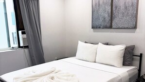 Moderni makuuhuone, jossa on sänky, ikkuna verhoilla, seinälle asennettu ilmastointilaite ja kaksi abstraktia maalausta.