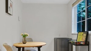 A small, modern kitchen with a dining table and chairs, a refrigerator, and a window with a view of trees. - Cozy and Calm: Modern Studio with Private Entrance (Vancouver)
