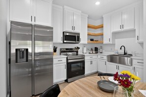 A modern kitchen with stainless steel appliances, white cabinetry, and a wooden dining table. - Modern Brownsville Duplex Near Zoo & SPI (Brownsville)