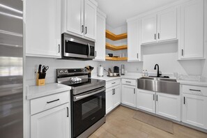 A modern kitchen with white cabinets, stainless steel appliances, and a wooden accent wall. - Modern Brownsville Duplex Near Zoo & SPI (Brownsville)