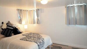 Un dormitori amb un llit, cortines, una làmpada i una manta decorativa.