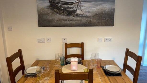 A dining table with chairs, a candle, and wine glasses set for four. - Cosy Cottage Sleeps 8 in Newburgh, Cupar, Fife (Newburgh)