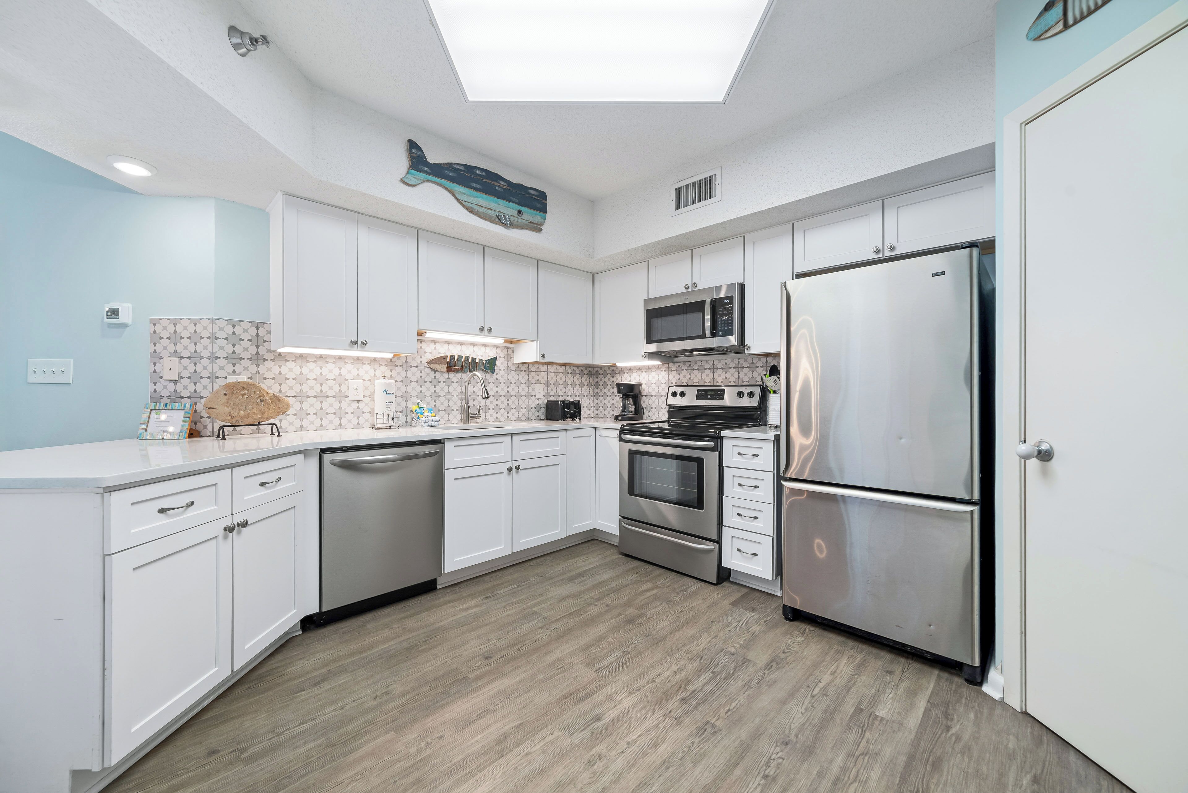 A modern kitchen with white cabinets, stainless steel appliances, and a skylight.