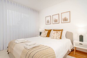 Ein ordentlich bezogenes Bett mit einer beigen und weißen Tagesdecke, zwei Kissen mit Blumenmuster und ein Nachttisch mit einer Lampe.